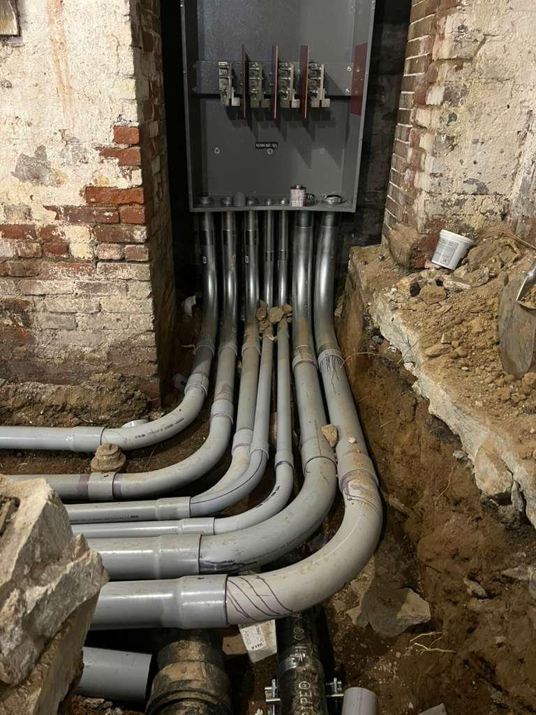 Grouped conduit sweeps rising from a trench into a commercial distribution enclosure