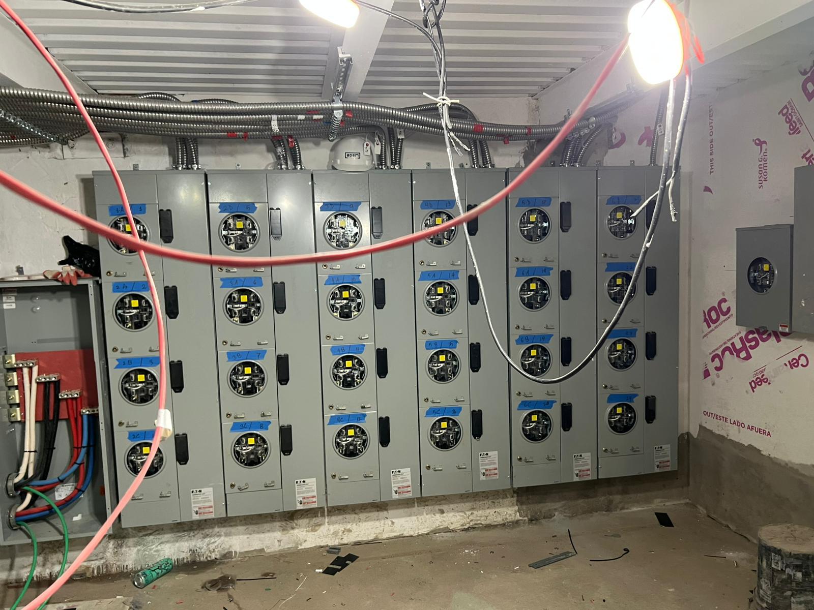 Rows of commercial meter stacks and distribution panels mounted in a building electrical room