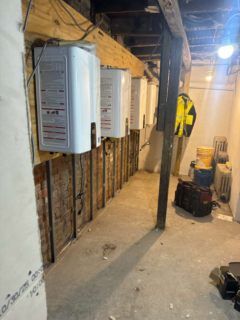 Wall-mounted tankless boilers and mechanical rough-in installed by AGC in a building cellar