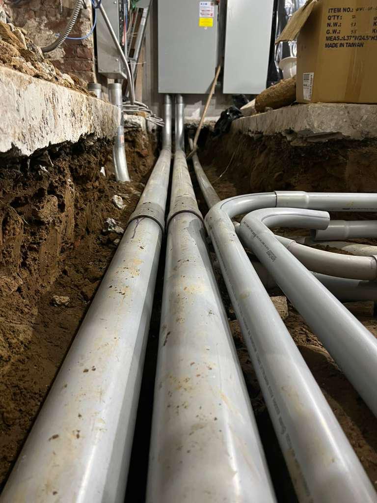 Parallel runs of large-diameter electrical conduit in a trench leading to wall-mounted equipment