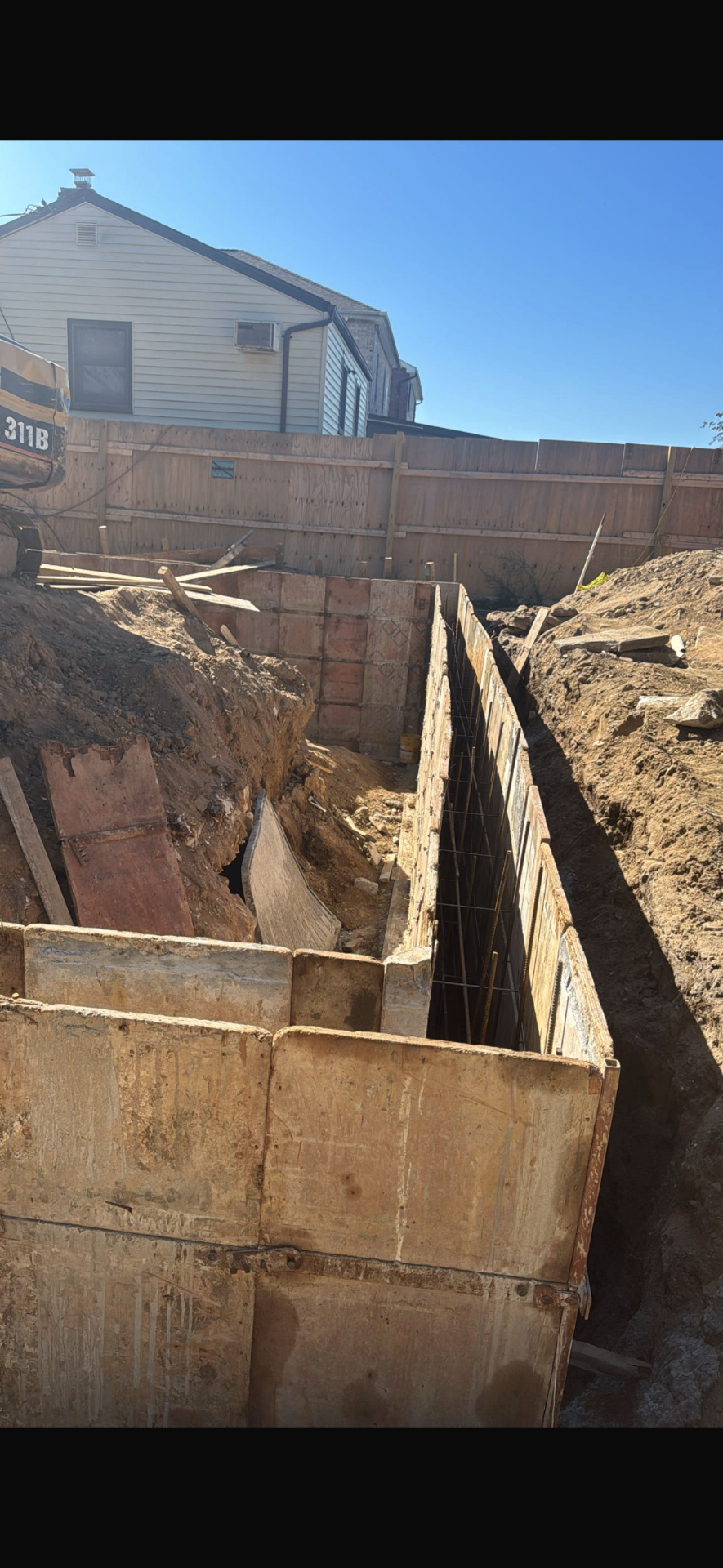AGC foundation wall formwork and rebar set in a shored excavation beside an existing house