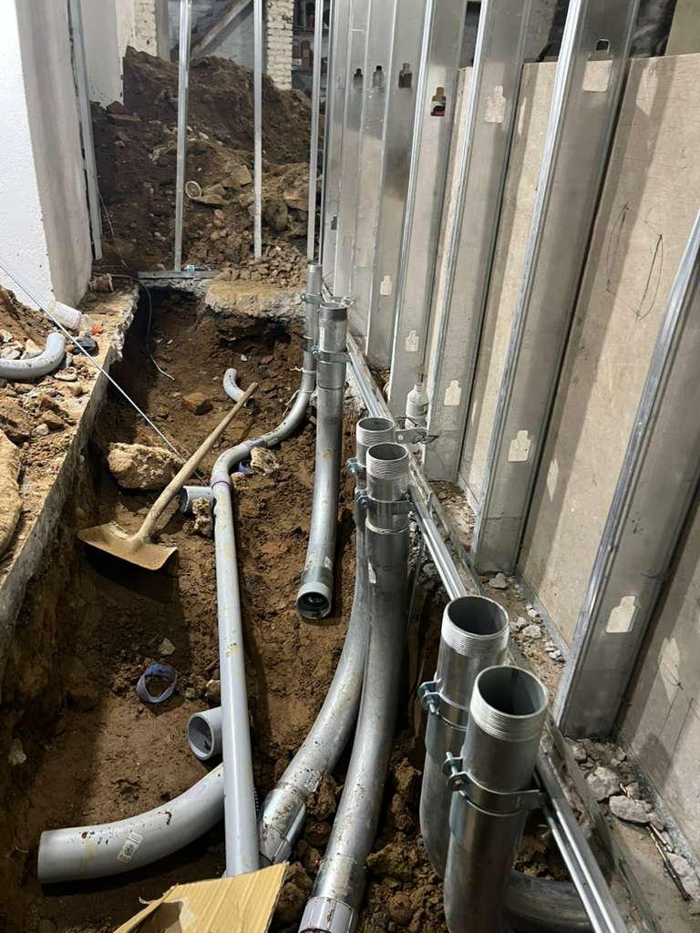 Underslab electrical and drainage conduit installed along a trench next to steel stud framing
