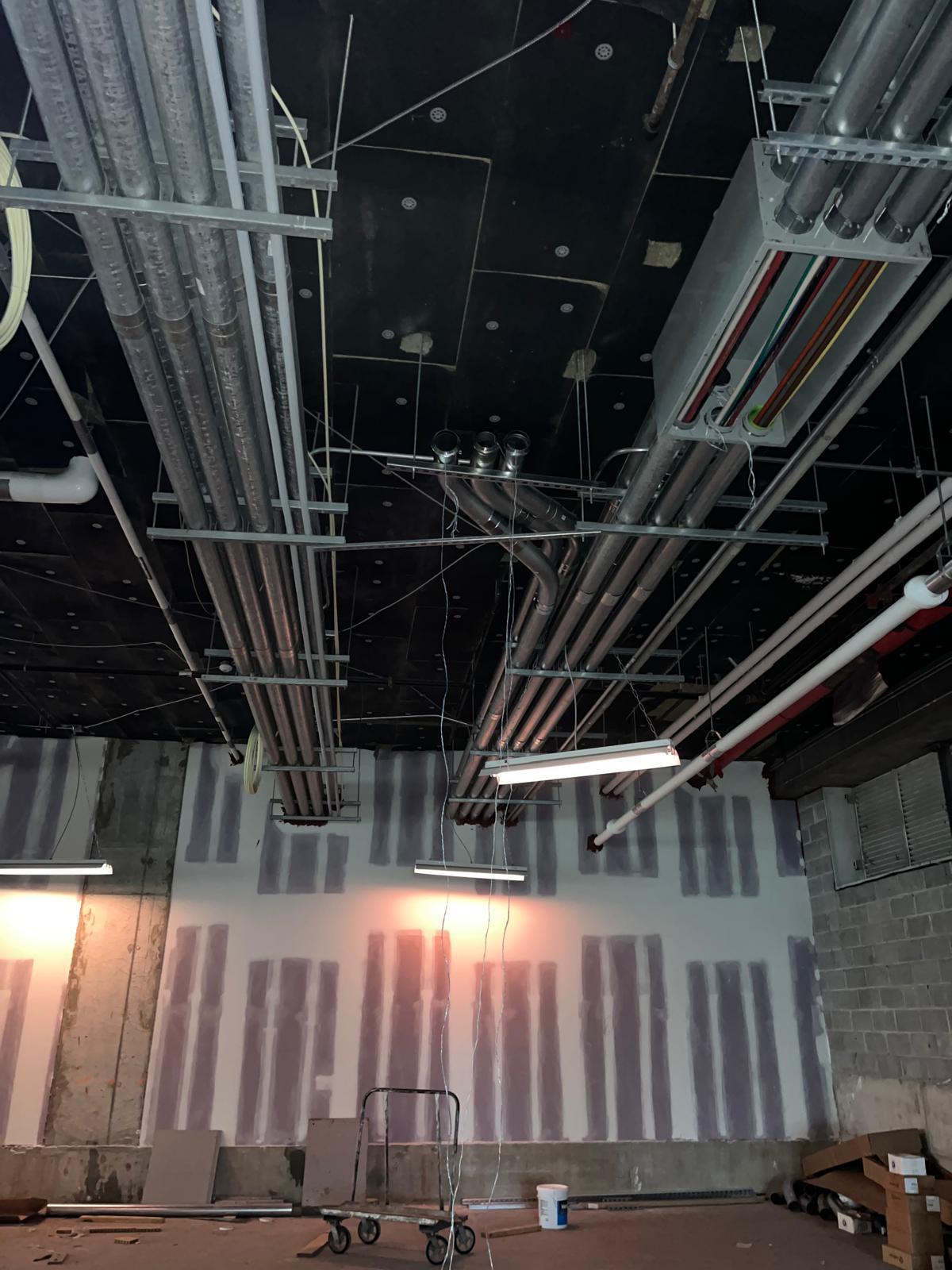 Overhead conduit, cable tray, and mechanical piping racked across an open commercial ceiling